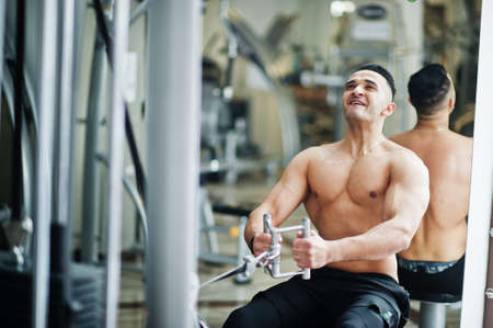 Muscular arab man training in modern gym. Fitness arabian men with naked torso doing exercises.
