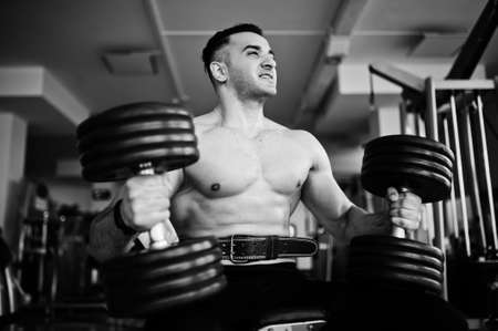 Muscular arab man training in with dumbbells modern gym. Fitness arabian men with naked torso doing workout.の写真素材