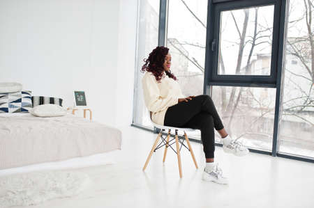 African woman in hoodie sit on chair at home.の写真素材