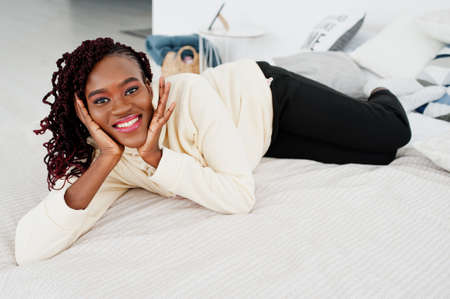 African woman in hoodie lying on the bed at home.の写真素材