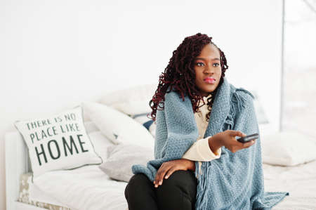 African woman watching tv at home and holding a remote control on bed.の写真素材