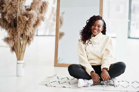 African woman in hoodie pose near mirror indoor with dry flowers.