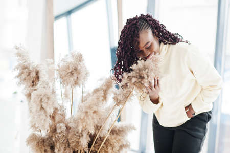 African woman in hoodie pose near mirror indoor with dry flowers.の写真素材