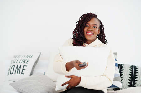 African woman watching tv at home and holding a remote control on bed.の写真素材