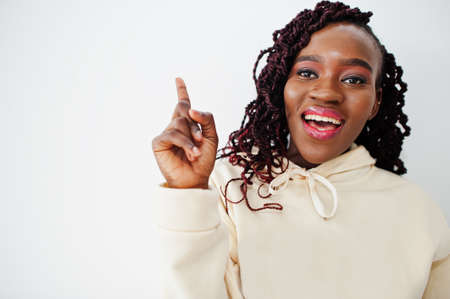 I got idea! African woman in hoodie stand against white wall and show finger up.