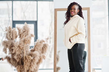 African woman in hoodie pose near mirror indoor with dry flowers.の写真素材