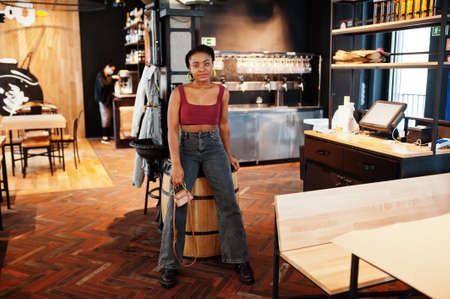 African woman in red marsala top and jeans posed indoor.