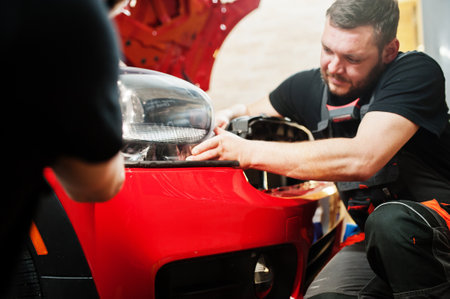 Car service worker put anti gravel film on a red car body at the detailing vehicle workshop. Car protection with special films.の写真素材
