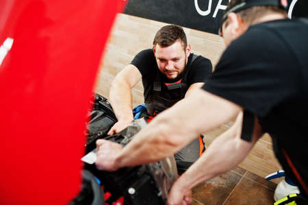 Car service worker put anti gravel film on a red car body at the detailing vehicle workshop. Car...