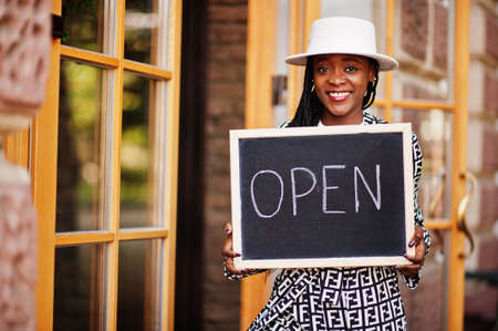 African american woman hold open welcome sign board in modern cafe coffee shop ready to service,...