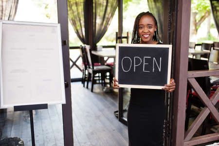 African american woman hold open welcome sign board in modern cafe coffee shop ready to service, restaurant, retail store, small business owner.の写真素材