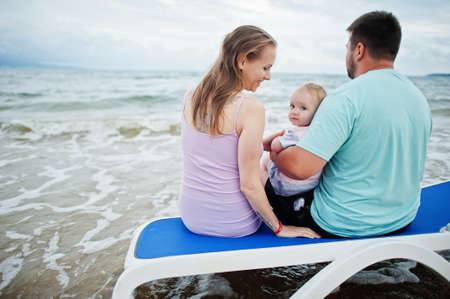 Summer vacations. Parents and people outdoor activity with children. Happy family holidays. Father, pregnant mother, baby daughter sitting on sunbed at sea sand beach.の写真素材