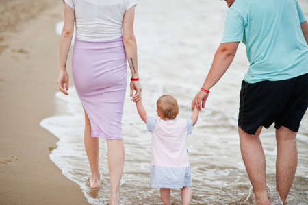 Summer vacations. Parents and people outdoor activity with children. Happy family holidays. Back view of father, pregnant mother, baby daughter on sea sand beach.の写真素材