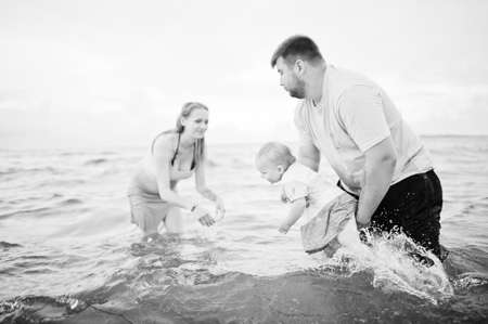 Summer vacations. Parents and people outdoor activity with children. Happy family holidays. Father, pregnant mother, baby daughter on sea sand beach.の写真素材