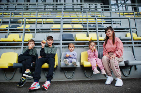 Young stylish mother with four kids sitting on chairs at the stadium. Family spend free time outdoors.の写真素材