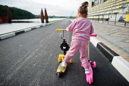 Back of baby girl in pink sport suit rides two scooter.の写真素材