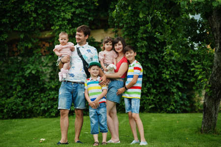 Beautiful large family with young parents and four kids stand in green grass at courtyard.の写真素材