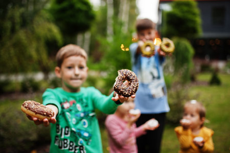 Four kids with donuts at evening yard. Tasty yummy donut food.の写真素材