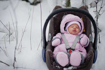 Baby girl toddler in car chair at winter day. In the park on cold day with snow.の写真素材