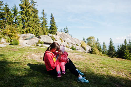 Charming motherly love. Mother with daughter sit on mountains against stone rocks.の写真素材