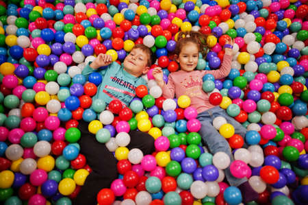 Brother with sister playing in colorful ball pit. Day care indoor playground. Balls pool for...