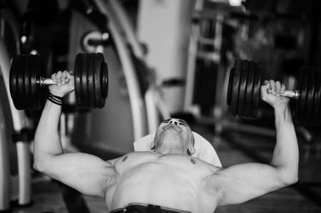 Muscular arab man training in with dumbbells modern gym. Fitness arabian men with naked torso doing...