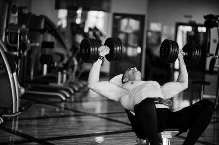Muscular arab man training in with dumbbells modern gym. Fitness arabian men with naked torso doing workout.の写真素材