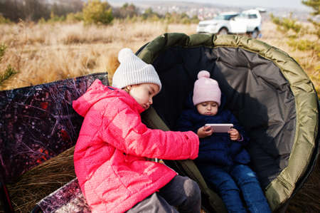 Two sisters sitting on chair outdoor picnic and watching cartooons on mobile phone.