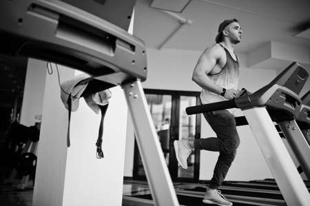 Fit and muscular arabian man running on treadmill in gym.