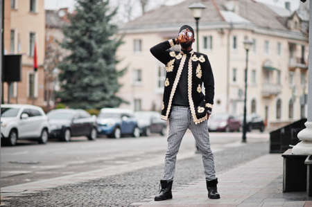 Mega stylish african man in traditional jacket pose. Fashionable black guy in hat and sunglasses with cigar in hand.の写真素材
