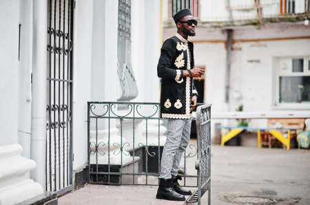 Mega stylish african man in traditional jacket pose. Fashionable black guy in hat and sunglasses...