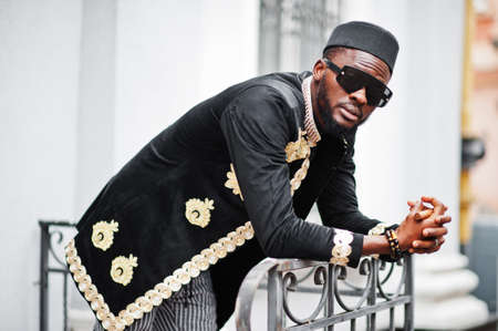 Mega stylish african man in traditional jacket pose. Fashionable black guy in hat and sunglasses with cigar in hand.の写真素材