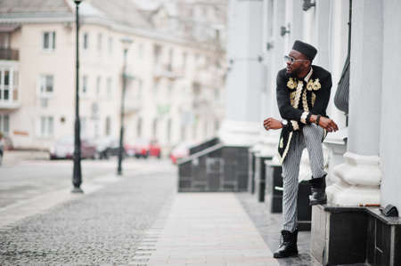 Mega stylish african man in traditional jacket pose. Fashionable black guy in hat and sunglasses.