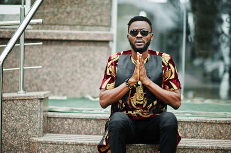 African stylish and handsome man in traditional outfit and sunglasses pray outdoor.の写真素材