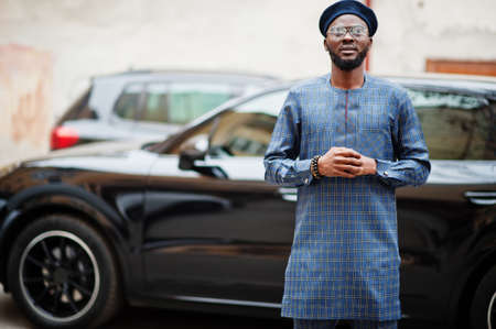 African guy in blue authentic costume, eyeglasses and beret. Fashionable nigerian man near black suv car.の写真素材