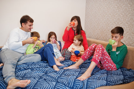 Happy big family is having fun together in bedroom. Large family morning concept. Four kids with parents wear pajamas drink tea in bed at home.の写真素材