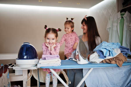 Woman mother and her two daughters child girls as little helper ironing at home.の写真素材