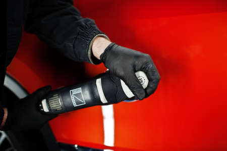Car detailing concept. Hands of man with orbital polisher in repair shop polishing orange suv car.