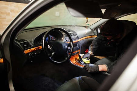 Man in uniform and respirator, worker of car wash center, cleaning car interior with hot steam...