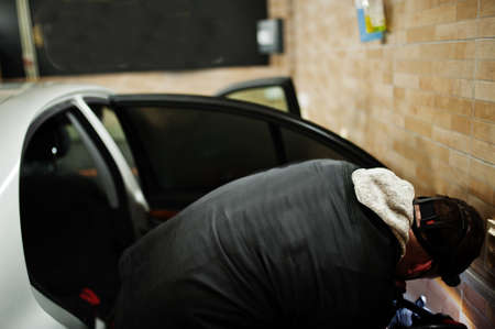 Man in uniform and respirator, worker of car wash center, cleaning car interior with hot steam...