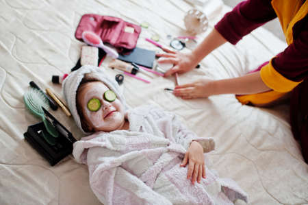 Mother with daughter in a bathrobe with a towel on her head take care of the skin at home, cucumbers on eyes.の写真素材