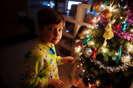 Kids looking on Christmas tree with shining garlands on evening home.