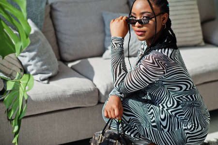 Afro woman in zebra dress sitting indoor. Stylish portrait of african american model in sunglasses.の写真素材