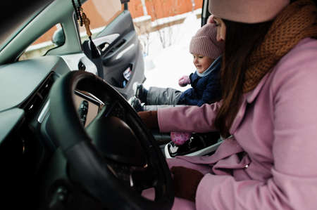 Young mother with baby girl daughter sit in electric car in the yard of her house at winter.