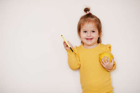 Baby girl in yellow with lemon and mobile phone, isolated background.の写真素材