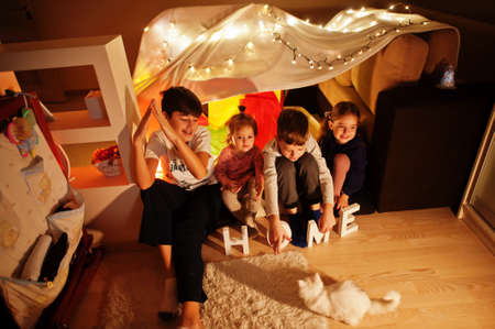 Playing kids with kitty in tent at night home. Hygge mood.の写真素材