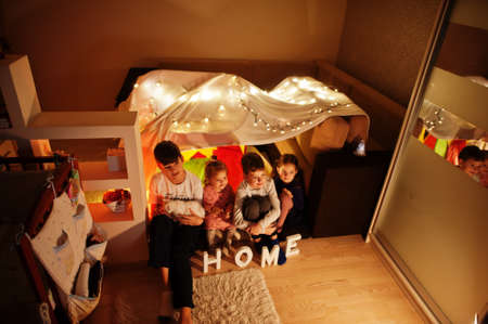 Playing kids with kitty in tent at night home. Hygge mood.の写真素材