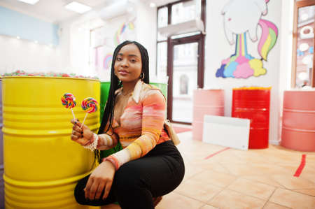 African american millennial lady at candy shop with lolipops.