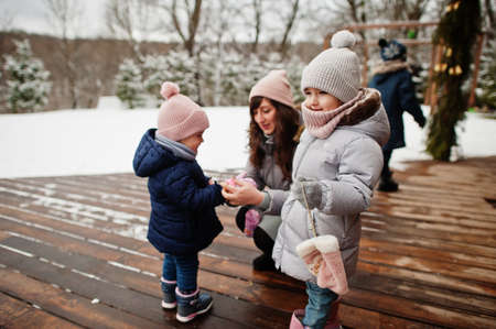 Attractive mother with her two pretty daughters in winter day. Mom puts on a baby glove.の写真素材