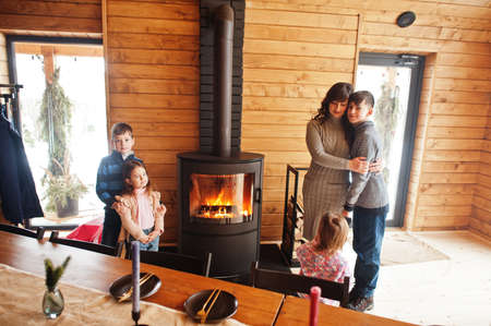 Mother and four kids in modern wooden house against table and fireplace, spending time together in warm and love.の写真素材